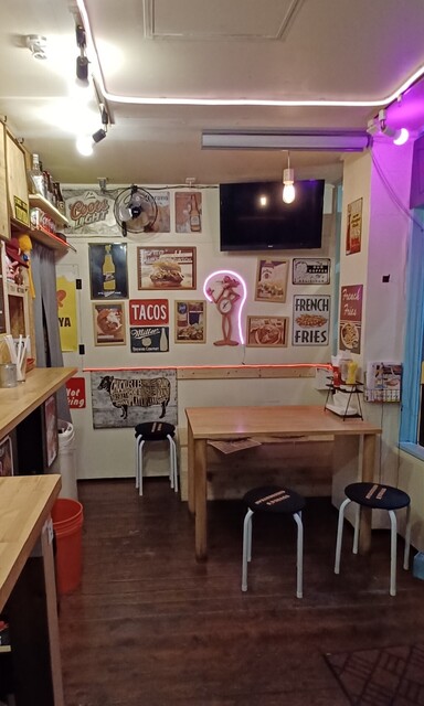 レトロなアメリカンダイナー調の小さな店内。壁のポスターとピンクのネオン、カウンター席
