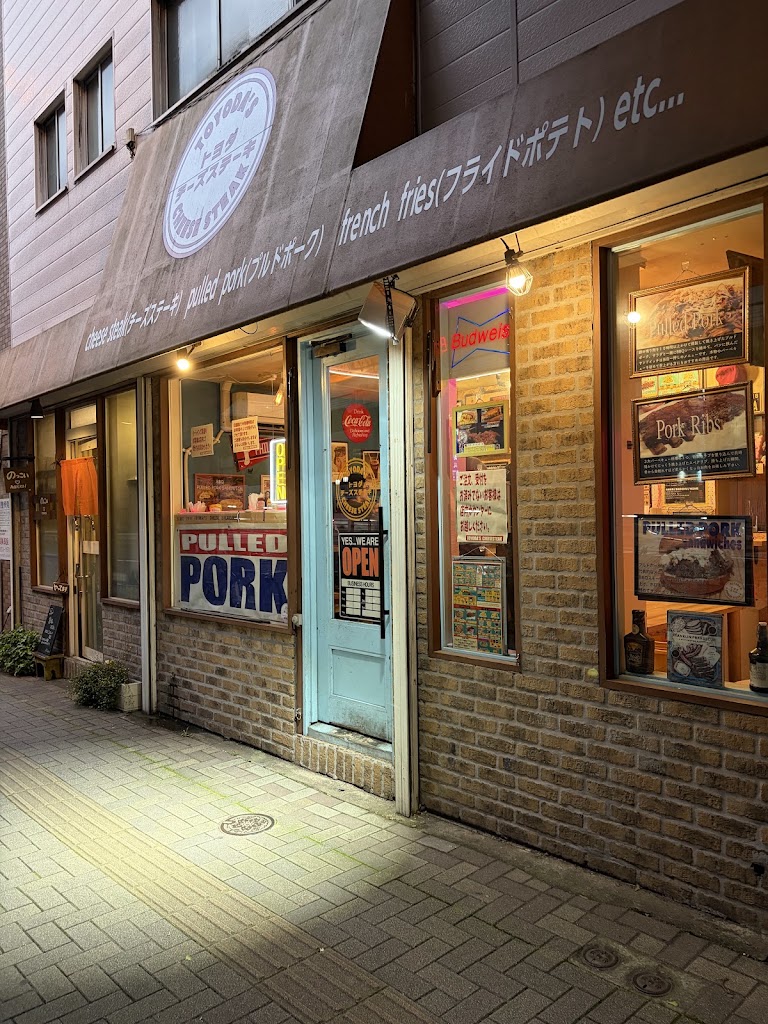 夜の店頭。ロゴのオーニングと『PULLED PORK』の窓看板、OPENのサイン